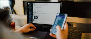 Person in front of a laptop holding a mobile phone